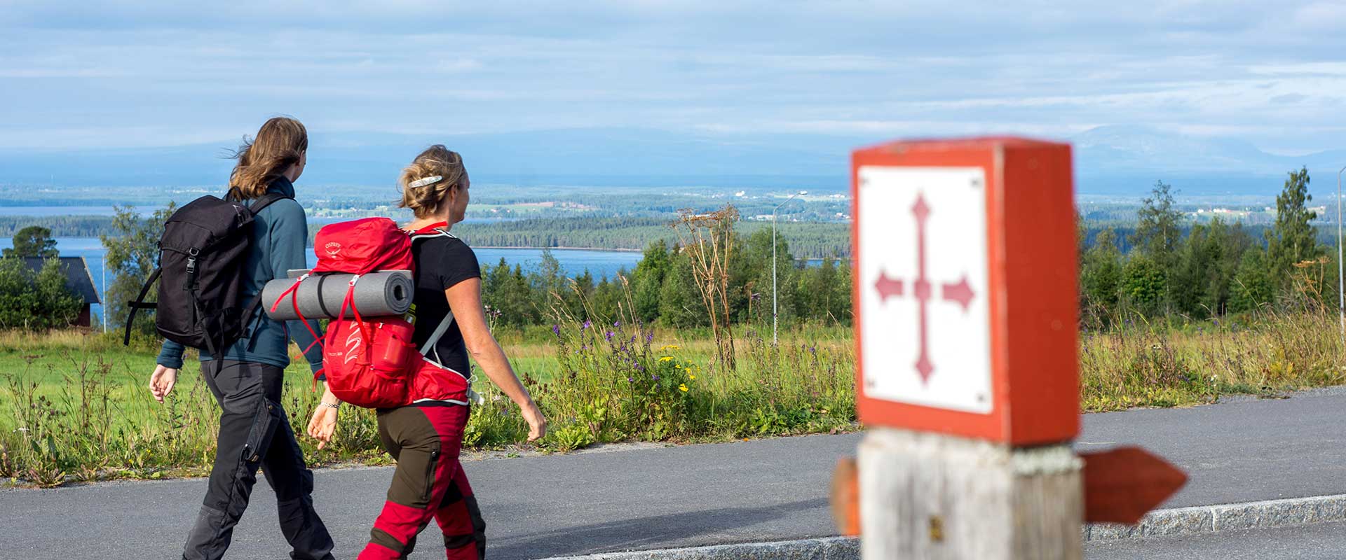 Två kvinnor vandrar förbi en S:t Olavsledenskylt